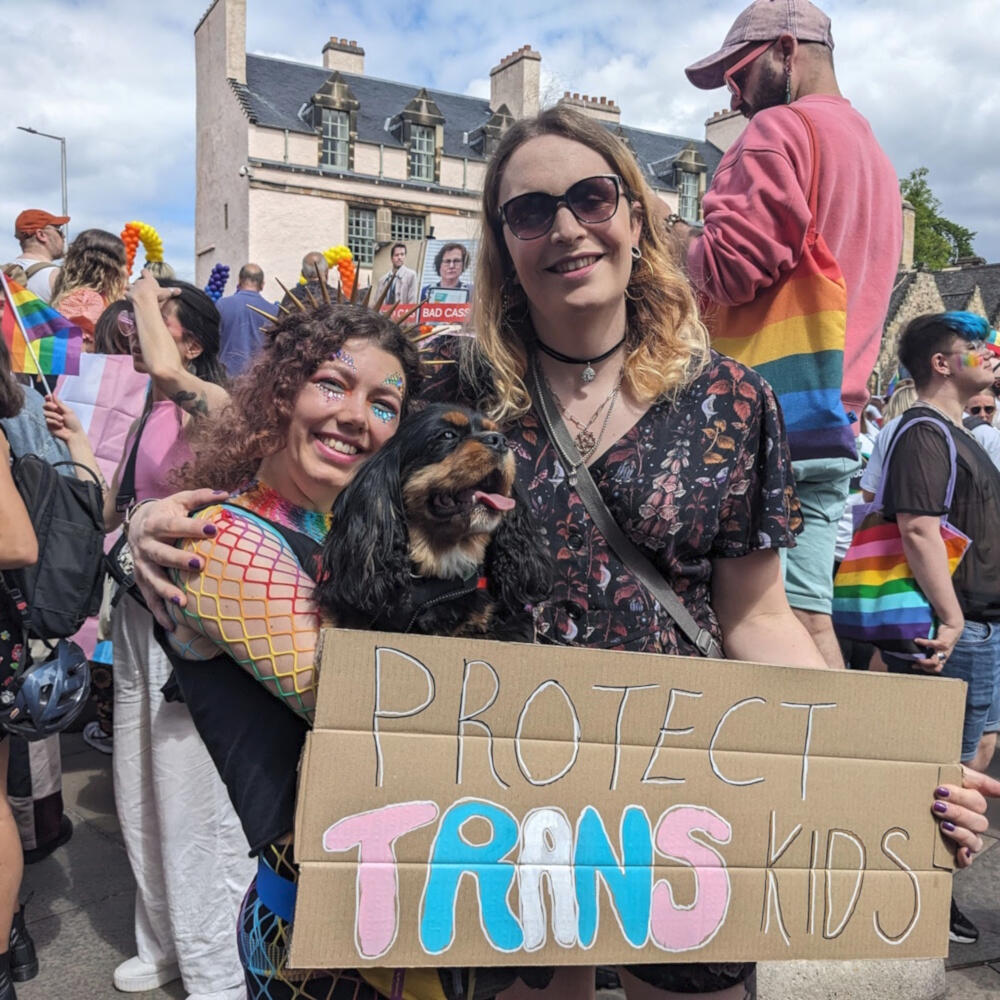 Empowering Queer Causes Lucy at Pride, holding a sign that says Protect Trans Kids